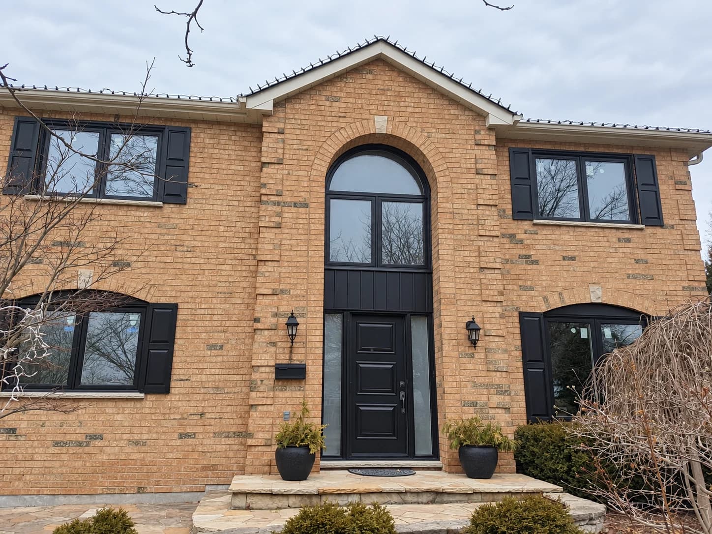 Brick home with black-framed windows and an arched window above the entrance