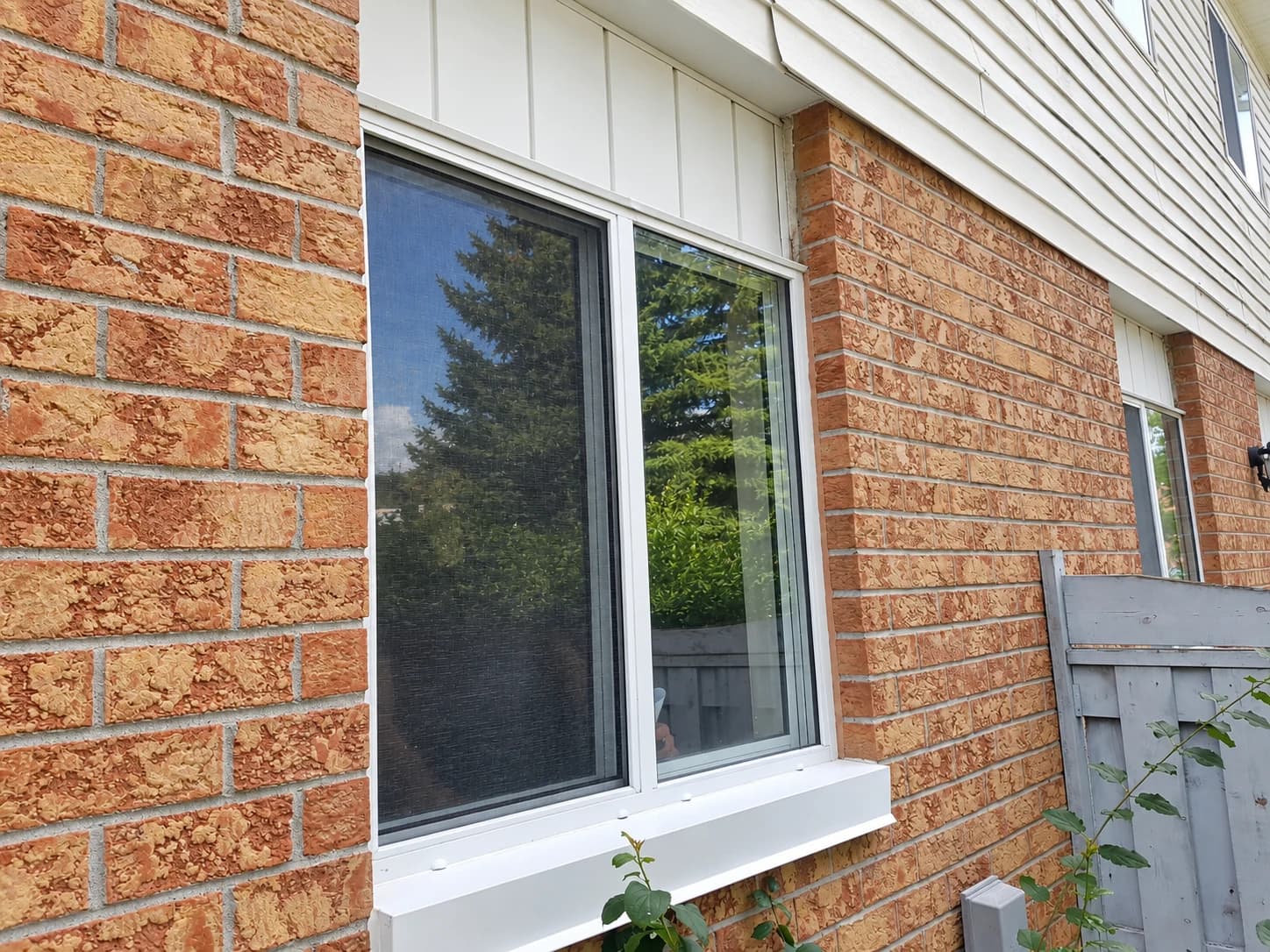 White sliding window with two glass panels and a brick exterior view